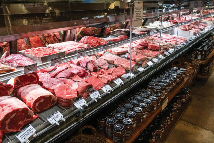 Butcher case filled with a variety of fresh cuts of beef and other meats, with jars of sauces displayed on shelves below.