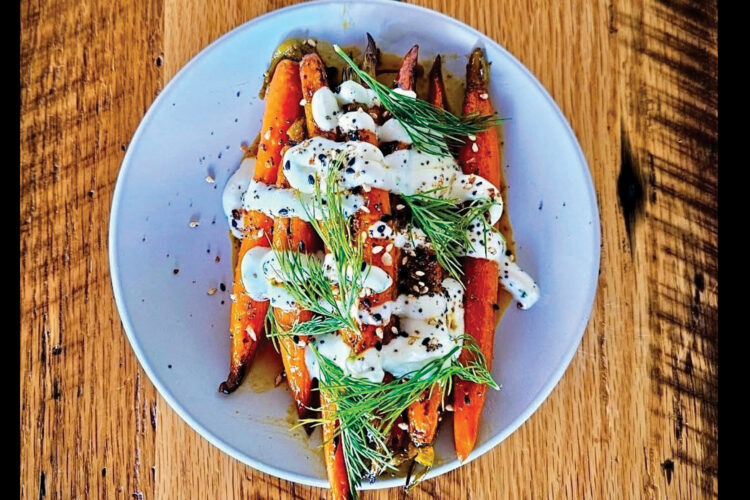 Roasted carrots topped with a creamy sauce, fresh dill, seeds, and seasonings on a light blue plate.