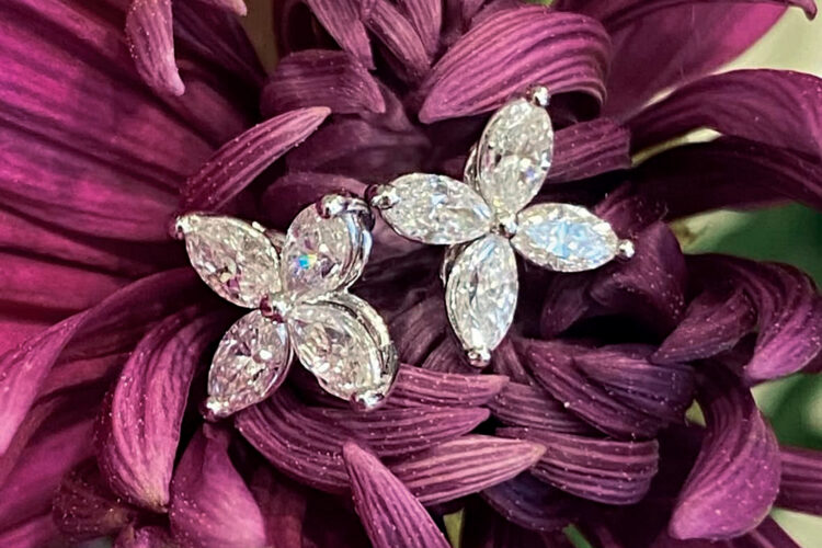 Pair of sparkling floral-shaped diamond earrings nestled among deep purple flower petals.