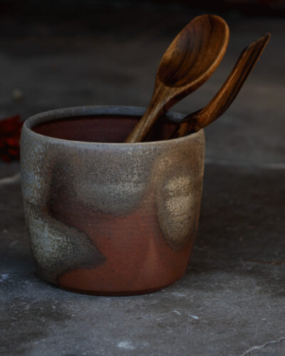 Earthy ceramic utensil holder from Twisted Pine Pottery holding two wooden spoons.