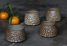 Four ceramic cups from Twisted Pine Pottery with pebble-like textures beside oranges.