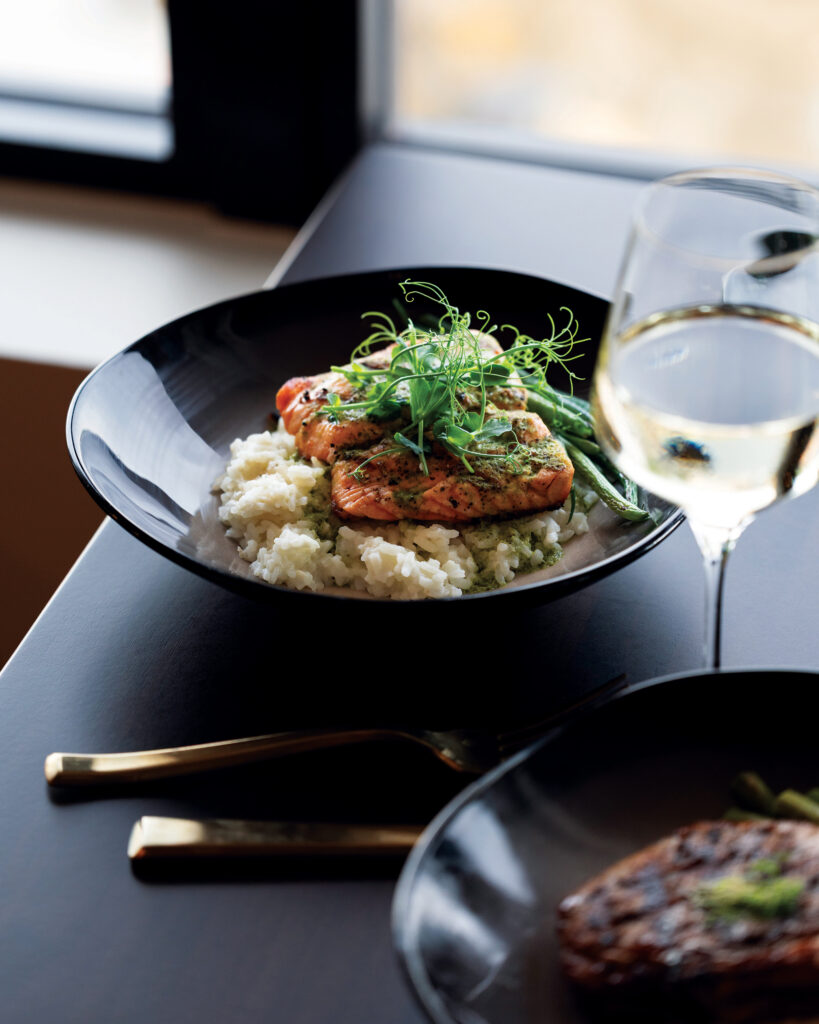 Salmon over rice with green vegetables beside a glass of white wine at Longmont Supply.