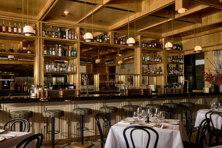 Wood-paneled bar with globe pendant lights and patterned stools at Petit Trois Aspen.