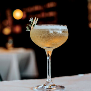 Petit Trois Aspen’s pear cocktail in a coupe glass with a small floral garnish.