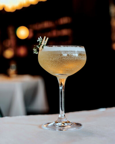 Petit Trois Aspen’s pear cocktail in a coupe glass with a small floral garnish.