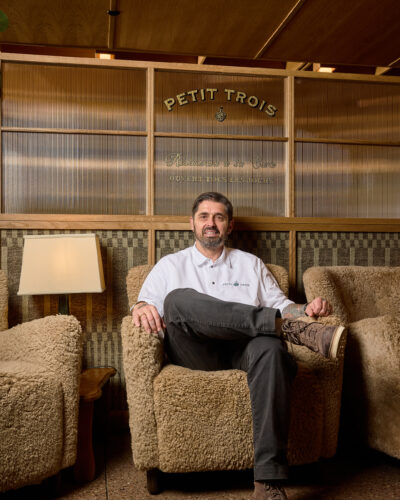 Chef Ludo Lefebvre seated in a textured armchair beneath the Petit Trois sign.