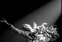 “DIVA” Takes the Denver Art Museum Stage Black and white photo of a performer holding flowers and a microphone with one arm outstretched.