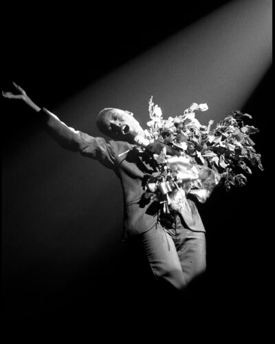 Black and white photo of a performer holding flowers and a microphone with one arm outstretched.