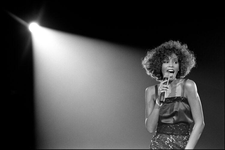 Black and white photo of a singer holding a microphone beneath a stage spotlight.
