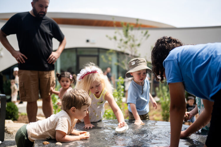 Children gather around an outdoor water play table at Anythink Nature Library in Thornton.