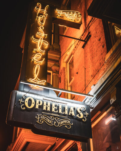 Ophelia’s Electric Soapbox sign beneath a glowing neon hotel sign in Denver.