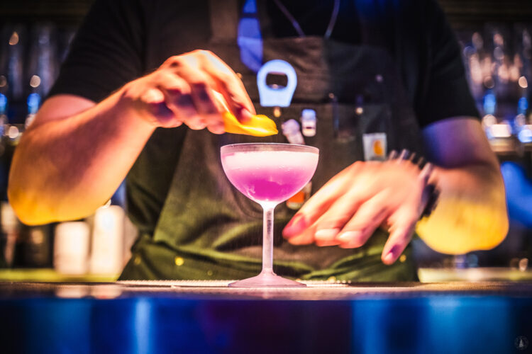 Bartender garnishes a pink cocktail with citrus peel at Ophelia’s Electric Soapbox.