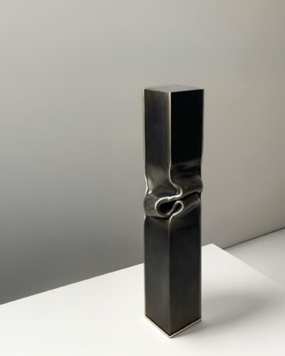Tall rectangular metal sculpture with a folded, pinched center on a white pedestal.