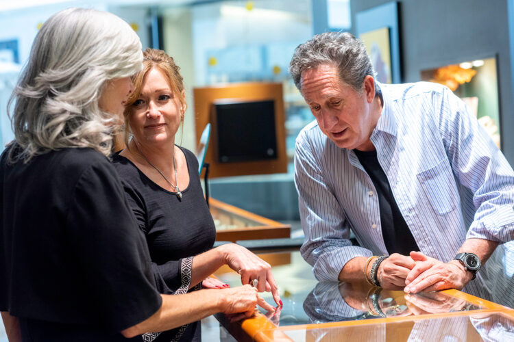 John Atencio and two women examining jewelry at a glass display counter.
