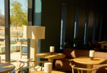 Boulder’s East & Co. Goes Beyond the Restaurant Sunlit seating area at East & Co. in Boulder with round wooden tables, woven chairs, and a rust-colored sofa.