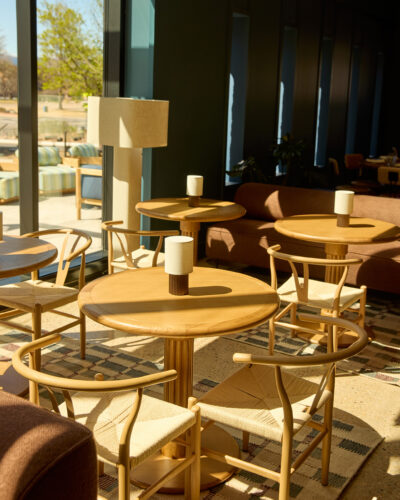 Sunlit seating area at East & Co. in Boulder with round wooden tables, woven chairs, and a rust-colored sofa.