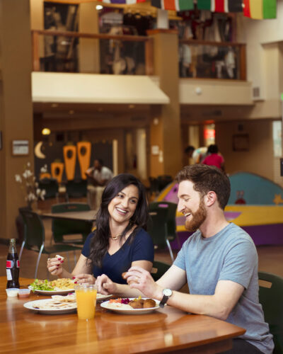 Two diners laugh over plates of food beneath international flags at Mango House in Aurora.