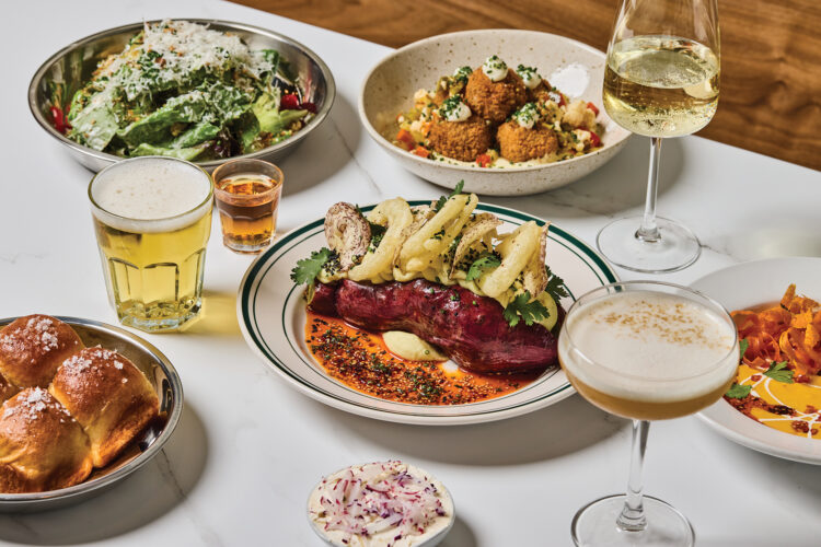 Plant-based dishes, bread rolls, salad, and drinks cover a table at Mother Other in Denver.