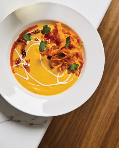 Orange soup topped with crisp vegetable ribbons, cilantro, and swirls of sauce.
