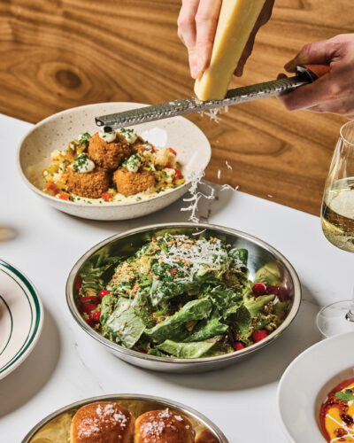 Hands grate a plant-based topping over a leafy salad at Mother Other.