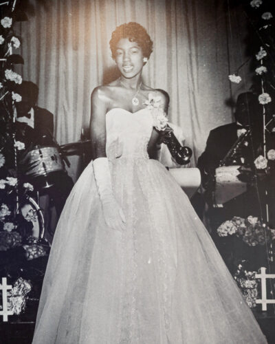 Archival black and white photo of a woman in a formal gown with musicians behind her.